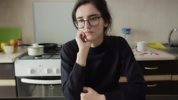 Bored Girl Is Sitting in the Kitchen with Glasses and Thinking About Something alt