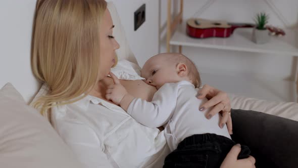 Young Blonde Woman Hugging and Feeding with Breast Her Baby Boy