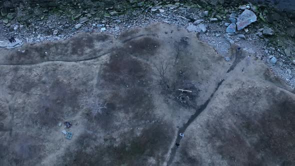 An aerial view over a park near a bay. The drone camera follows two people walking on a dirt path du alt