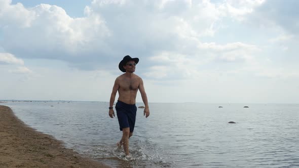 Happy Man in Shorts and Cowboy Hat Walks on the Beach