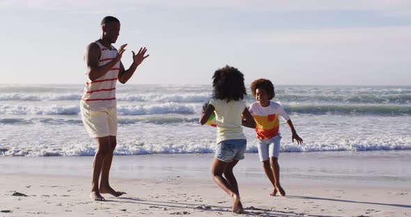 African american father and his children playing with a ball on the beach alt