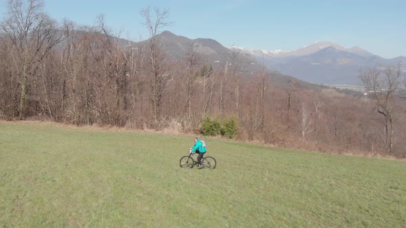 Aerial slow motion: man having fun by riding mountain bike in the grass on sunny day, scenic alpine alt
