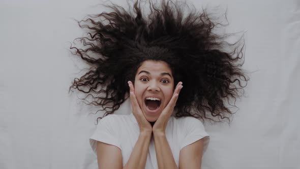 Top View of Excited Young African American Girl in Pajamas Lies on the Bed in Awe Says Wow alt