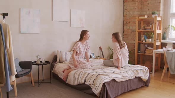 Happy Twin Sisters Sitting on Bed and Chatting alt