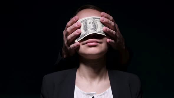 Money blinds a woman in a business suit, causing a smile. Danger of money alt