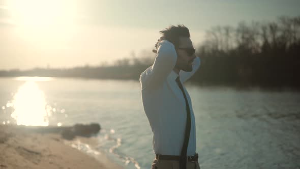Guy In Sunglasses Walks On Sand And Dreaming. Man Walking On City Beach. Man Walking On Sand Beach. alt