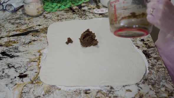 Spooning the cinnamon and brown sugar mix on the dough to make cinnamon rolls - side view zoom alt