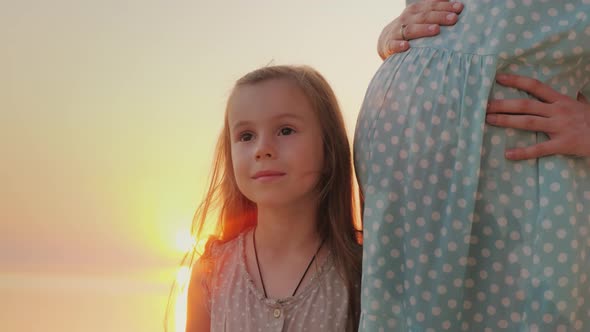 A Little Girl Is Standing Near the Belly of Her Pregnant Mother alt