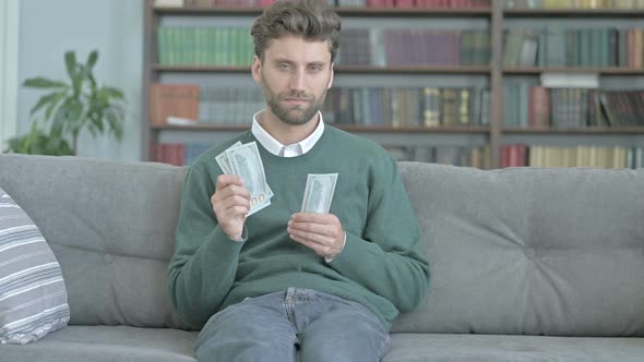 Young Man Sitting on Sofa and Counting the Money alt