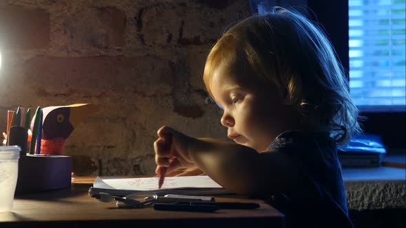 Lefty Little Girl Sits Near The Window And Painting. Baby Is Painting In The Album With Lamp Light.