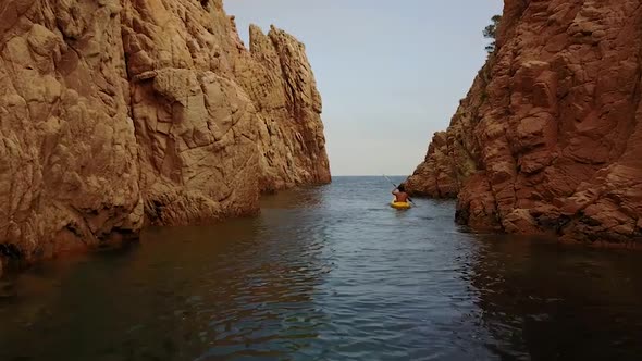 Flying behind a young man kayaking through mediterranean cliffs on a cloudy day