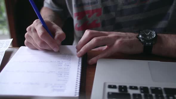 Close-up of man writing in notebook with laptop computer nearby