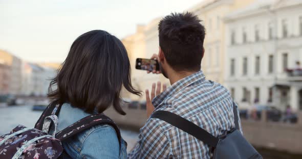 Back View of Young Couple on Holidays Taking Selfie on Cellphone in Foreign City alt