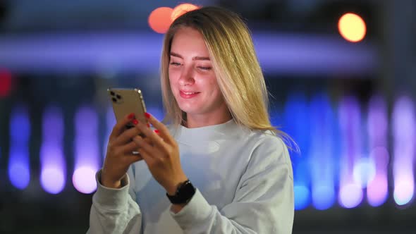 Woman Messaging on Phone at Night on the Street With the Lights of the Road Blurred Background. alt
