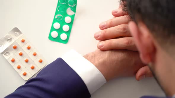 Pills and man with his head on the table. alt