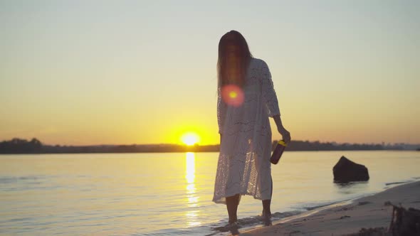 Back View of Slim Young Woman in White Gown Drinking Wine From Bottle at Resort. Wide Shot of alt