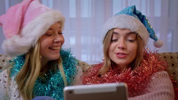 Portrait of Beautiful Cheerful Girls in Santa Caps Congratulates Their Friends By Video Call. Young