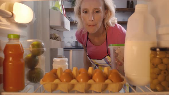 Mature Woman Taking Eggs From Fridge in Kitchen alt