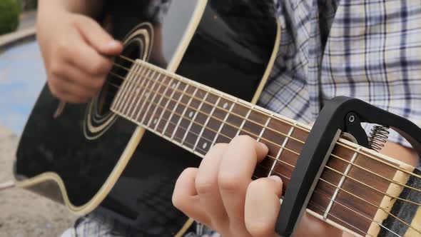a Teenager Plays an Acoustic Guitar Rearranging the Chords on the Strings and Fixing the Capadastr