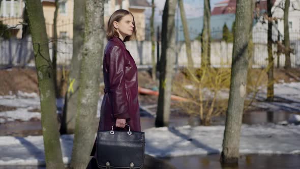 Side View Elegant Slim Female Detective Walking in City Park on Sunny Winter Day Thinking alt