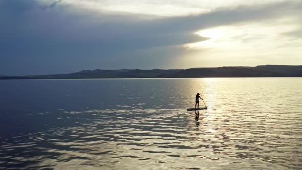 Drone Shot of a Woman with Long Hair Surfing on a Mountain Lake at Sunset