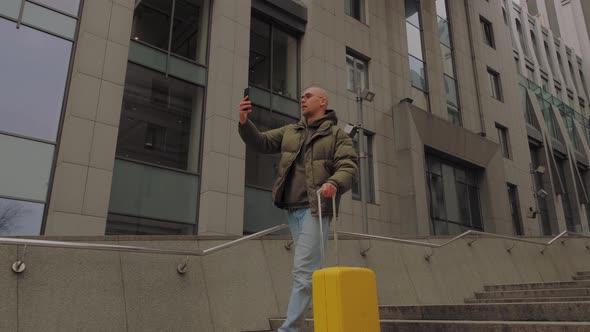 Young European Man Going with Yellow Suitcase and Talks on the Phone alt