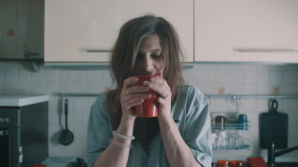 Attractive Woman Drinking Coffee Out Red Mug and Smiles in Kitchen at Morning