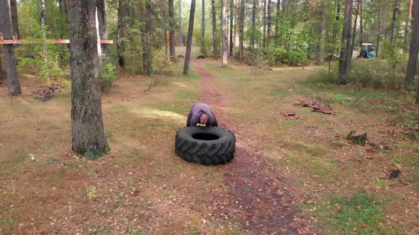 A Tough Man Bodybuilder Pushes Over the Tire on the Ground in the Autumn Forest alt