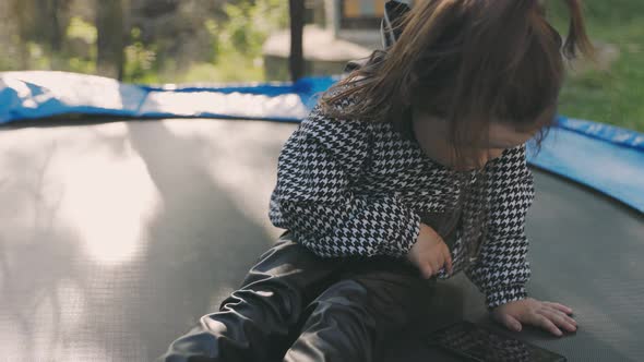 Girl Looking at the Phone While Sitting on a Trampoline alt