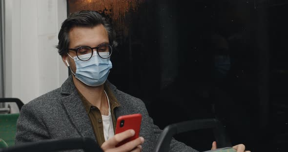 Male Person in Wireless Earbuds Listening To Music and Touching Screen While Sitting in Public