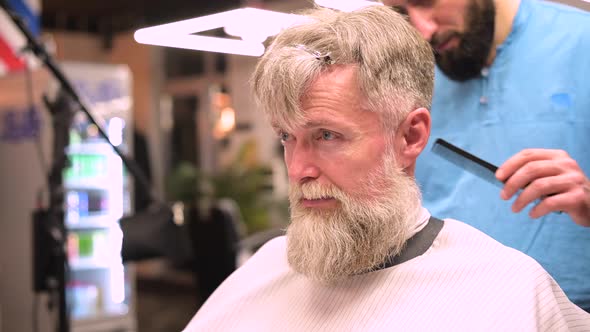 Gray-haired adult bearded man gets a haircut from a barber alt