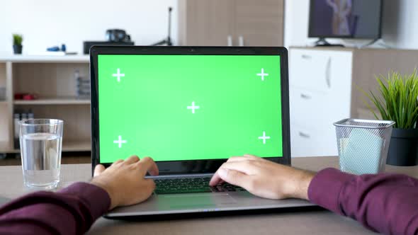 Male Hands Typing on the Laptop with a Mock Up Green Screen Chroma in the Living Room alt