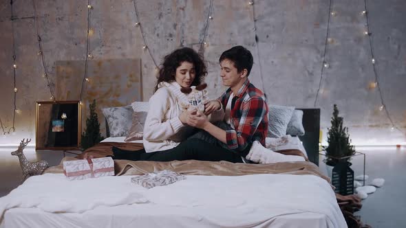A Couple in Love in Winter Sweaters and Thick White Socks Are Sitting on the Bed alt