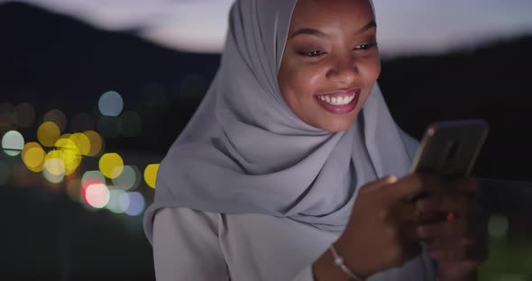 Muslim Woman Texting on Smartphone with Bokeh City Light in Background alt