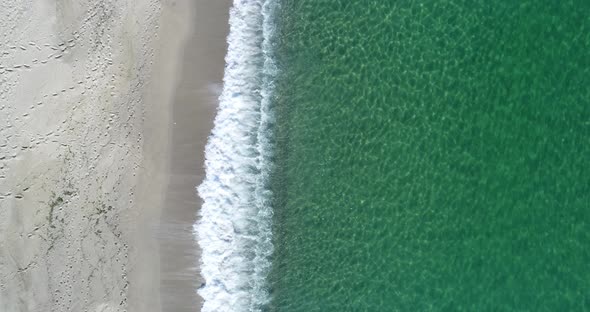 Static top down view of tropical beach, foamy ocean waves washing sand. Waves hitting sand beach alt