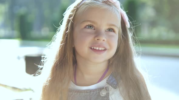 Portrait of pretty child girl standing outdoors in summer park smiling happily. alt