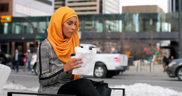 Side view of young Asian woman in hijab eating food in the city 4k alt