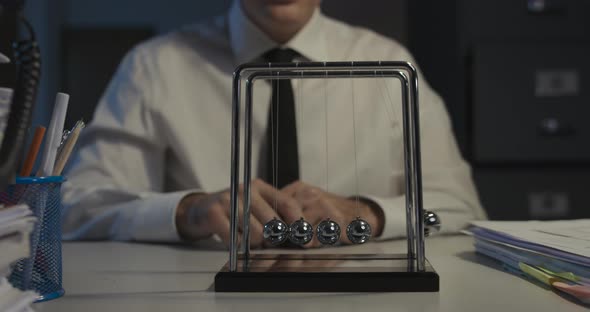 Sad office worker sitting at desk and staring at Newton's cradle balls