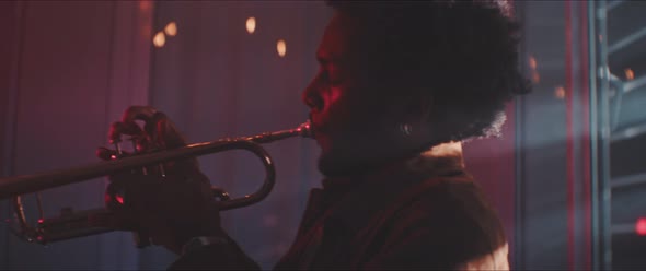 Professional trumpeter playing in a room with smoke and red neon light alt