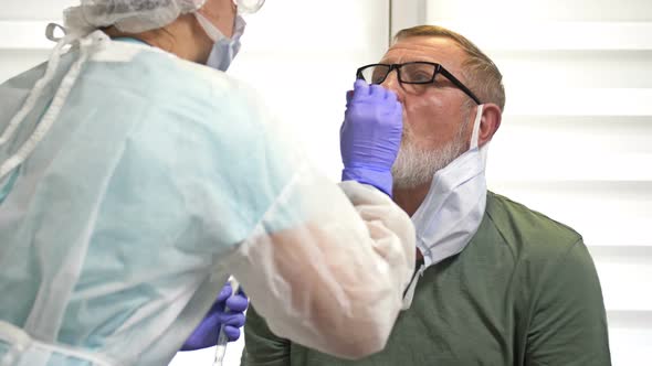 Lab Technician in a Protective Suit Takes a Swab From an Elderly Patient for Coronavirus alt