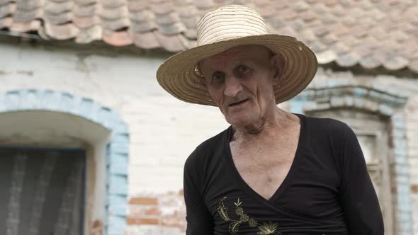 Old Man with Wrinkled Face Stands Near Shabby House Wall