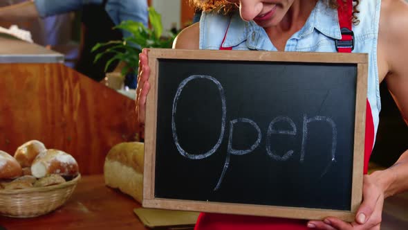 Female staff holding a open sign slate in supermarket alt