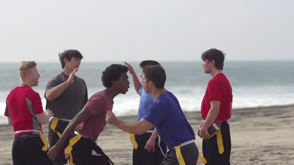 A group of guys playing flag football on the beach. alt