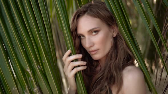 Beautiful young woman posing with palm leaves