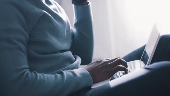 Closeup View of Hands of a Guy Using a Laptop Placed on His Lap and Holding Phone alt