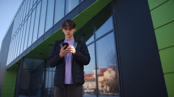 Shot of Handsome Young Man Working on Smartphone Stands on the Street in Front of a Modern Building