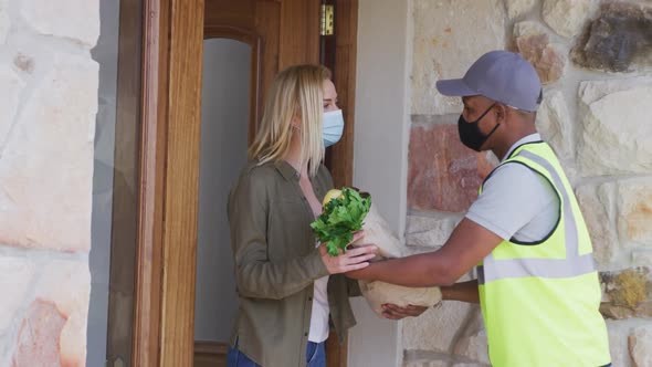 Delivery man delivering groceries to woman wearing face mask at home alt