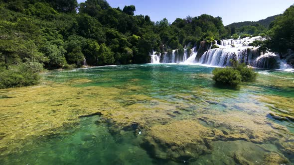 Tilt up from colorful water to wide waterfalls and forest at Krka alt