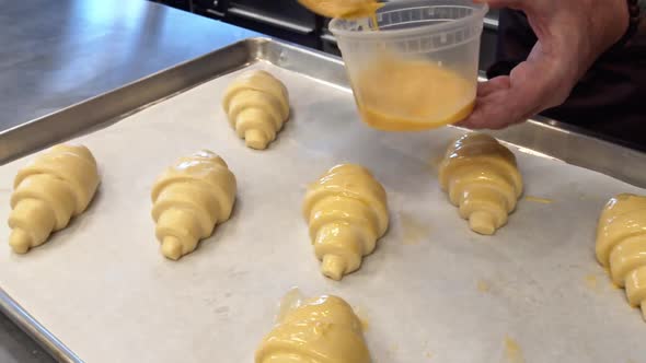 A Baker painting Egg wash on to croissants that will be baked in a cafe alt