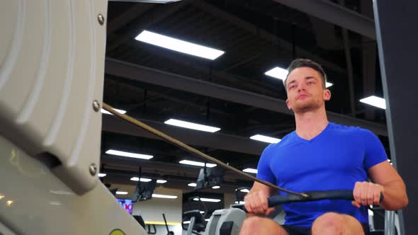 A Young Fit Man Trains on a Rowing Machine in a Gym - Closeup alt